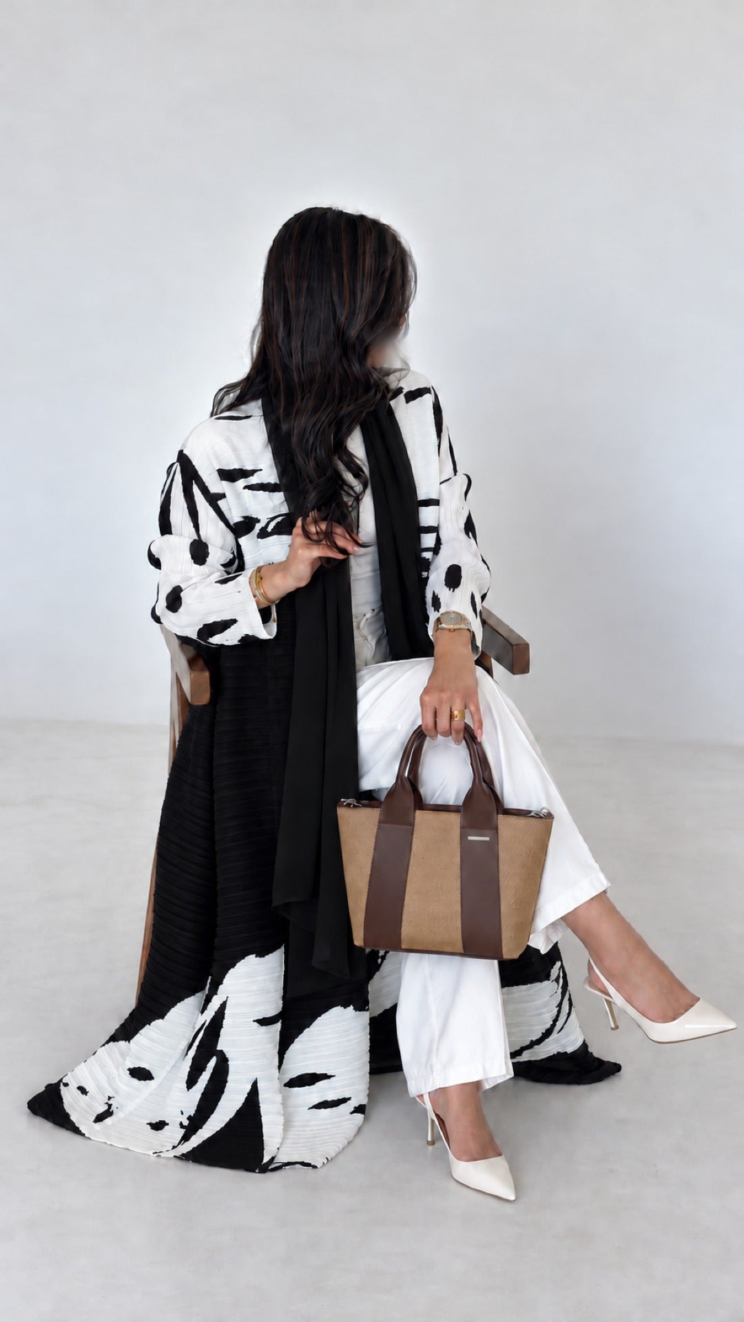 Reem Top-Handle Bag in brown, resting on the knee while seated